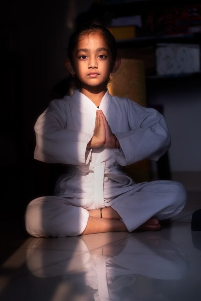 A young girl in a white gi meditates in sunlight.